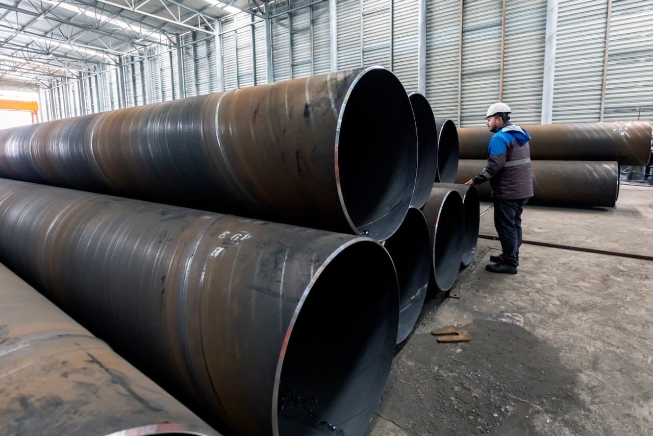 Almacenamiento de tubos de acero en un taller industrial, con un trabajador inspeccionando los materiales.