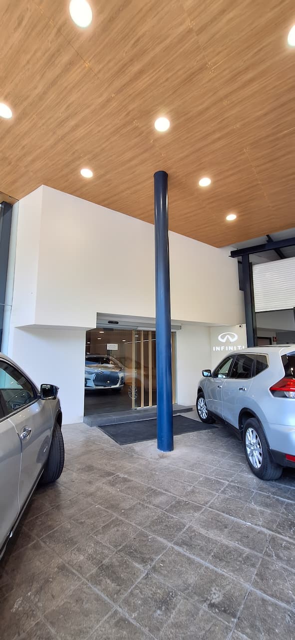Entrada de un concesionario de automóviles con un diseño moderno, mostrando vehículos estacionados y una iluminación cálida en el techo.