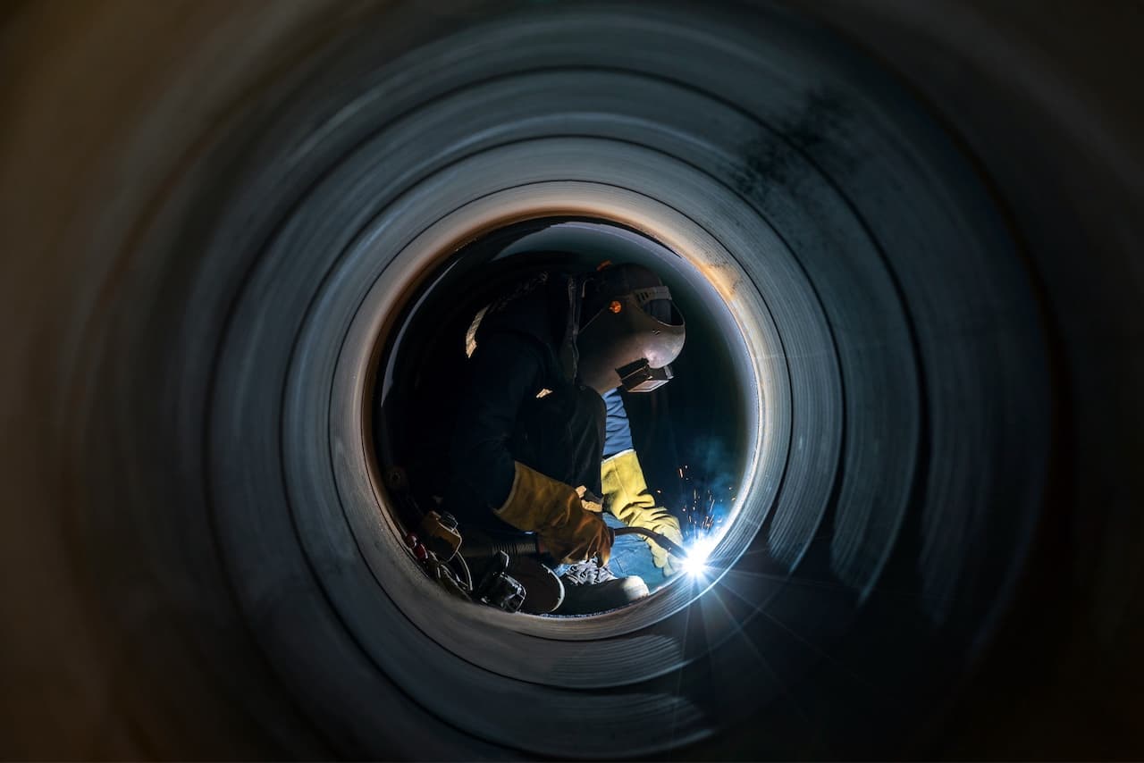 Un soldador trabajando en el interior de un tubo, generando chispas y luz.