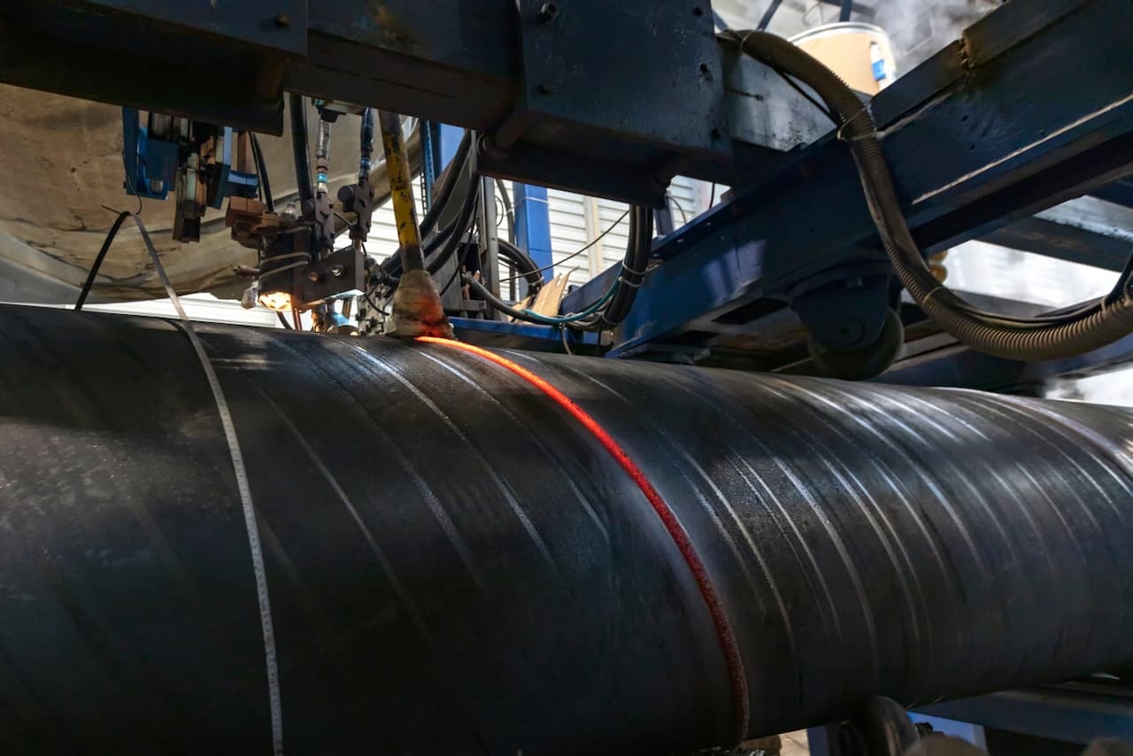 Proceso de soldadura de una tubería de gran diámetro, con un foco de luz roja indicando el área de unión.