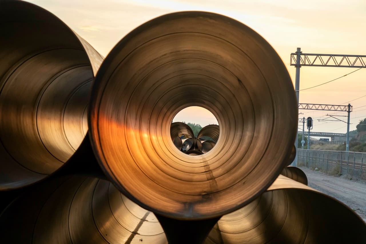 Tuberías de acero apiladas con una vista hacia el horizonte y un cielo iluminado al atardecer.