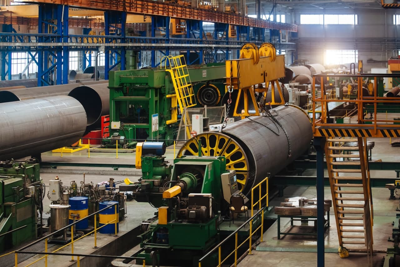 Fábrica con maquinaria para la producción de tubos de acero, grúas y equipos de procesamiento en un entorno industrial.